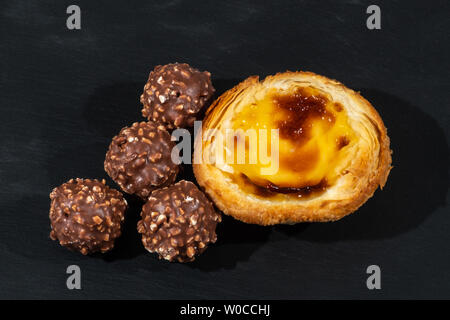 Zitrone Custard Pie mit Vier nussig Schokolade Eis Kugeln, serviert auf einem Schwarzen, schiefergedeckt, Platte Stockfoto
