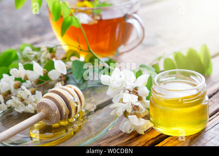 Akazie blumen Honig Glas, Holz- Pendelarm und gesunde Kräuter Tee Tasse. Stockfoto