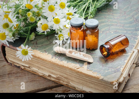 Kamillenblüten, Flaschen der homöopathischen Kügelchen und alte Bücher. Stockfoto