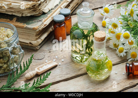 Infusionsflaschen, Kamillenblüten und Thuja occidentalis Pflanze, Flaschen der homöopathischen Kügelchen und alte Bücher. Stockfoto