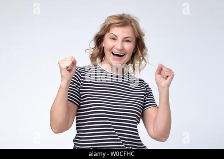 Reife Glück europäische Frau aufgeregt und glücklich halten Mund öffnete und die Fäuste. Studio shot auf weißem Hintergrund. Stockfoto