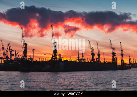 Schwarze Silhouetten von Kränen und Schiffen im Hamburger Hafen bei Sonnenuntergang Stockfoto