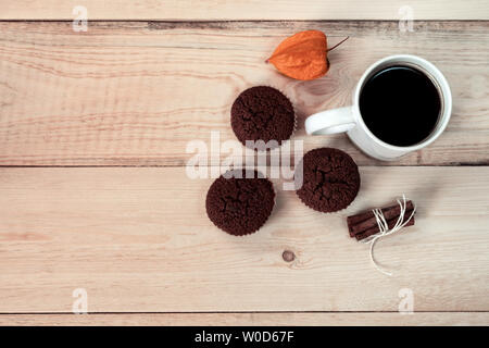 Eine weiße Tasse Kaffee mit drei Muffins, Zimt und Orange Blume auf einem Holzbrett. Ansicht von oben. Stockfoto