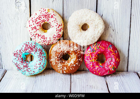 Fünf mehrfarbig glasierten Creme Donuts auf einem hölzernen Hintergrund sind in der Form von Ringen Olympische Symbolik gelegt. Spaß Leistung von vertrauten Thin Stockfoto