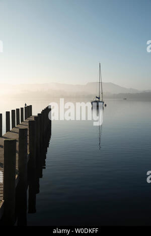 Schöne unplugged Landschaft Bild der Segelyacht sitzt immer noch in ruhigen See Wasser im Lake District während der friedlichen nebligen Herbst Sonnenaufgang Stockfoto