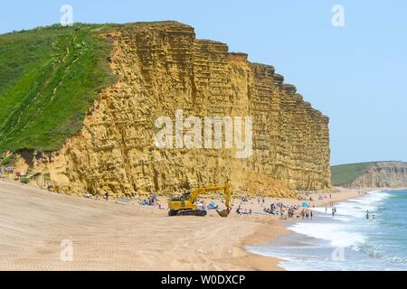 West Bay, Dorset, Großbritannien. 27. Juni 2019. UK Wetter. Sonnenanbeter auf dem offenen Abschnitt der Strand unter den Felsen am Strand von West Bay in Dorset, genießen Sie einen Tag mit strahlend blauem Himmel und glühend heiße Sonne. Der Hauptteil des Bech hat enge für die Umweltagentur Küstenschutz arbeitet. Foto: Graham Jagd-/Alamy leben Nachrichten Stockfoto