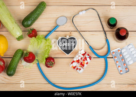 Tafel in Form von Herzen mit Text Übergewicht, Stethoskop und Wahl zwischen natürlichen Vitaminen, Gemüse, Obst und Beeren oder Tabletten und Pillen o Stockfoto