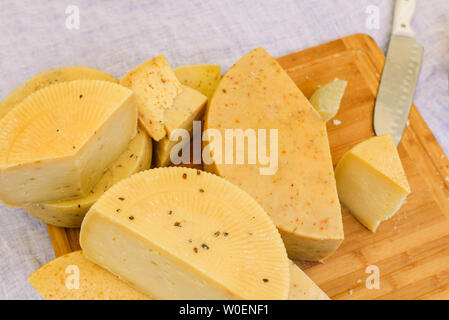 Scheiben Käse liegen auf einem Holzbrett Nahaufnahme. Verschiedene Sorten Käse, weiße Bettwäsche Tischdecke Stockfoto