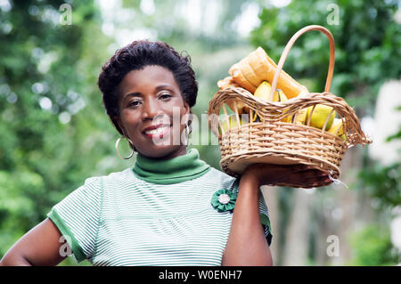 Lächelnde junge Frau mit einem Korb mit Obst in der hand und ging für ein Picknick Stockfoto