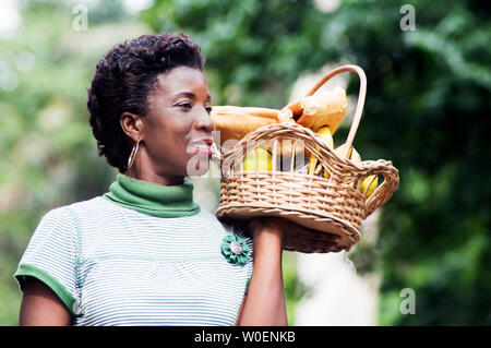 Lächelnde junge Frau mit einem Korb mit Obst in der hand und ging für ein Picknick Stockfoto