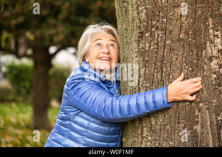 Porträt eines hübschen Senior Frau umarmt einen Baum. Stockfoto