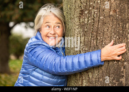 Porträt eines hübschen Senior Frau umarmt einen Baum. Stockfoto