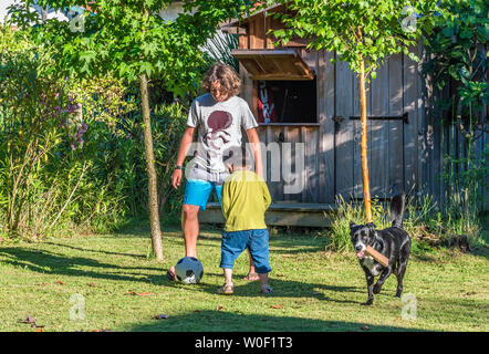 Zwei Jungen, der fünf Jahre alt ist und 13 Jahre alt, spielen mit einem Ball im Garten Stockfoto