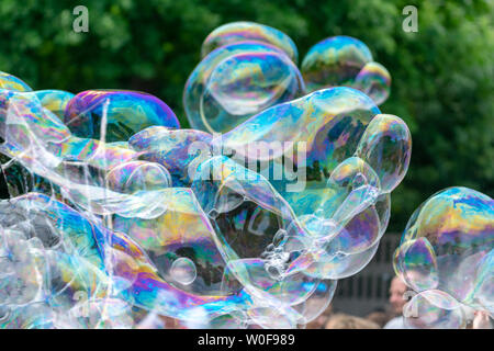 Seifenblasen mit bunten Reflexionen auf dem Hintergrund der grüne Bäume während der Kinder zeigen. Stockfoto