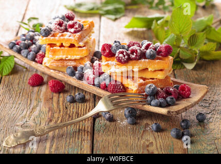 Waffeln mit Himbeeren und Blaubeeren auf einem alten Holztisch. Stockfoto