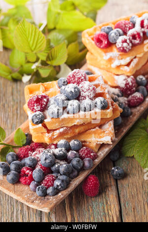 Waffeln mit Himbeeren und Blaubeeren auf einem alten Holztisch. Stockfoto
