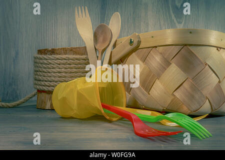 Bunte Plastikgabeln und kippten Weidenkorb auf rustikalen Holzmöbeln Hintergrund in Nahaufnahme. Recycling von Kunststoffen Konzept Bild Stockfoto