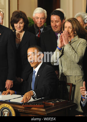 Us-Präsident Barack Obama nutzt die letzten Pen und sagt: "Es ist vollbracht" Unter dem Applaus der Sprecherin des Repräsentantenhauses Nancy Pelosi, wie er Zeichen der Health Insurance Reform Bill durch eingeladene Gäste und Mitglieder des Kongresses im East Room des Weißen Hauses in Washington, DC am 23. März 2010 umgeben. Hinter der Präsident ist Vicki Kennedy, die Witwe des ehemaligen Senator Ted Kennedy. Die historische 938 $ Mio. health care Bill wird für 32 Millionen unversicherten Amerikanern garantiert und berühren wird fast jeder amerikanischen Lebens. UPI/Pat Benic Stockfoto