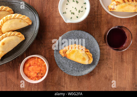 Empanadas mit Saucen und Wein, geschossen von oben auf einen dunklen Holzmöbeln im Landhausstil Hintergrund mit einem Platz für Text Stockfoto