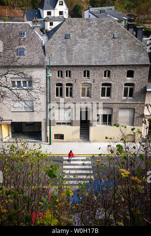 CLERVEUX, Luxemburg - 18. OKTOBER 2018: Frau mit roten Jacke überquert die Straße in Clerveux Stockfoto