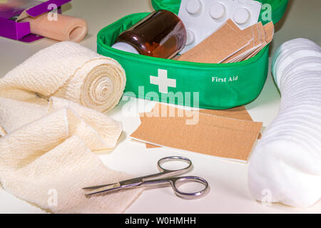 Inhalt einer Erste Hilfe Kit, bestehend aus einem gepolsterten Kasten und der Punkte, die auf eine Verletzung oder Wunde behandeln, nämlich, Verband, Pflaster, Watte und Schere. Stockfoto