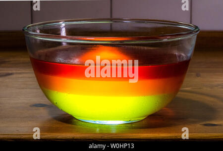 Nahaufnahme von einem großen Glas Schale mit drei Schicht Gelee / jello Nachtisch, bestehend aus Limone, Orange und Erdbeer, auf einem mit Pinien Küchenarbeitsplatte. Stockfoto