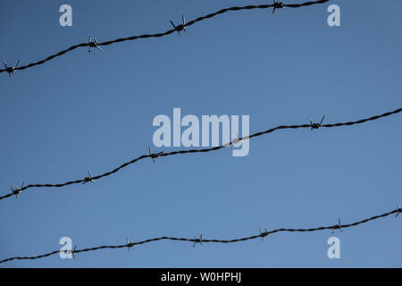 Drei Reihen von rostigem Stacheldraht vor einem blauen Himmel, abstrakten Stockfoto