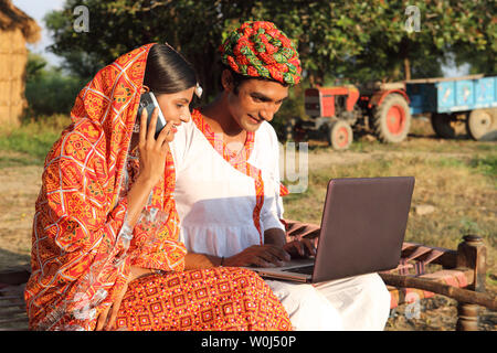 Indischen Bauern mit einem Laptop mit seiner Frau telefonieren mit einem Handy Stockfoto