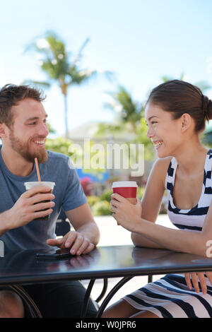 Cafe paar Spaß trinkt Kaffee reden Lächeln und Lachen am Tag im Sommer. Junger Mann mit asiatischen Frau sitzt im Freien. Gerne Freunde in der späten 20er Jahre. Stockfoto