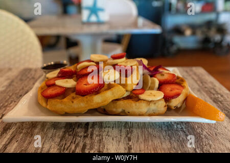 Knusprige golden Waffeln mit frischen Früchten wie Erdbeeren und Bananen in einer Low Angle View auf einem Schild an einem Restaurant Tisch lagen Stockfoto
