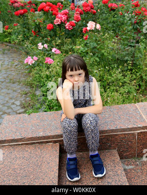 Kleines Mädchen sitzt auf dem Hintergrund der Garten Stockfoto