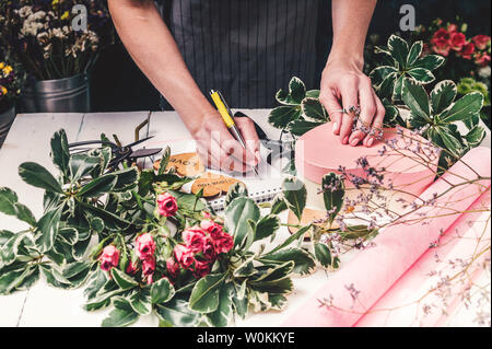 Blumengeschäft arbeitet. Frauen Hände schreiben Sie eine Bestellung einen Strauß Rosen und viel Grün. Small Business Konzept Stockfoto