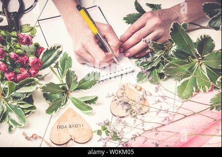 Blumengeschäft arbeitet. Frauen Hände schreiben Sie eine Bestellung einen Strauß Rosen und viel Grün. Small Business Konzept Stockfoto