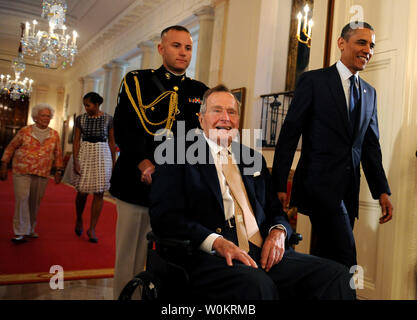 Us-Präsident Barack Obama geht mit ehemaliger Präsident George H.W. Bush im Osten Zimmer des Weißen Hauses zu den 5.000 th Award von Bushs 'Points of Light Foundation in Washington, DC am 15. Juli 2013 vorlegen. Bush hat die nationale Bewegung volunteerism und Dienst an der Gemeinschaft zu Vorauszahlung vor 20 Jahren, als er die 41. Präsident war. Im Hintergrund sind der First Lady Michelle Obama und ehemalige First Lady Barbara Bush (L). UPI/Pat Benic Stockfoto