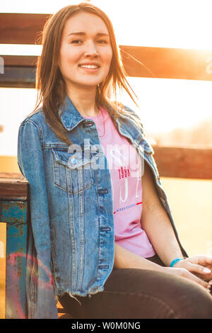Portrait der Attraktive, schlanke, schöne junge Kaukasier blondes Mädchen in einer Jeans Jacke und Pink t-shirt. Lächelnde Mädchen schönen warmen sunner Stockfoto