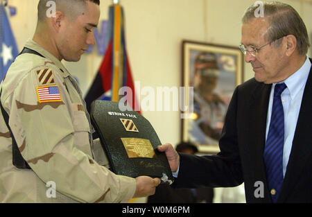 Armee SPC. Anthony Dowden des 3 Infanterie Division stellt eine Plakette von einem Stück von Rüstung, die ihn von einem Sniper bullet zu Verteidigungsminister Donald H. Rumsfeld in Bagdad, Irak vorgenommen, am 12. April 2005. Rumsfeld im Irak mit US- und Koalitionstruppen zu besuchen und mit den neu gewählten Mitgliedern der irakischen Regierung zu treffen. (UPI Foto/Cherie A. Thurlby/Air Force) Stockfoto