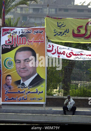 Ein ägyptischer Mann liest die Papier sitzt neben einem wahlplakat Für amtierende Präsident Hosni Mubarak in Kairo am 31. August 2005. Die Mehrheit der Kampagne Plakate und Banner erscheinen in Kairo werden von Anhängern des amtierenden Präsidenten als einen Akt der Loyalität und ihre Unterstützung für ihn während der bevorstehenden Präsidentschaftswahlen am 7. September 2005 zu demonstrieren. (UPI Foto/Stewart Innes) Stockfoto