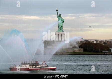 Ein New Yorker Feuerwehr Boot spritzt Wasser als die USS New York geht Ihr in der Nähe der Freiheitsstatue in New York am 7. November 2009. Das Schiff hat 7 1/2 Tonnen Stahl aus dem World Trade Center in seiner Hülle geschmiedet geborgen, soll am 7. November 2009 in Betrieb genommen werden. UPI/Danielle Speck/U.S. Marines Stockfoto