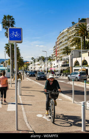 CANNES, Frankreich - April 2019: Person Radfahren auf einem Radweg entlang einer Straße auf der Promenade in Cannes. Stockfoto