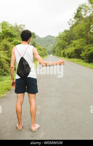 Junger Mann per Anhalter auf dem Berg Straße im Sommer Stockfoto