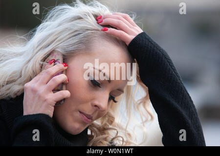 Umgekippt, junge Frau, die sich in einem mobilen läuft Ihre Hand durch Ihr langes lockiges Haar mit einem besorgten Ausdruck betont