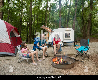 Mutter und Töchter camping rund um ein Lagerfeuer mit teardrop Wohnmobil und Zelt im Hintergrund. Stockfoto