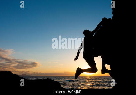 Klettern. Ein Kletterer Klettern (ohne Seil) auf die Küste Meer bei Sonnenuntergang. Stockfoto