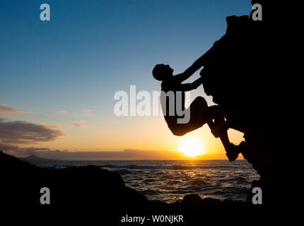Klettern. Ein Kletterer Klettern (ohne Seil) auf die Küste Meer bei Sonnenuntergang. Stockfoto