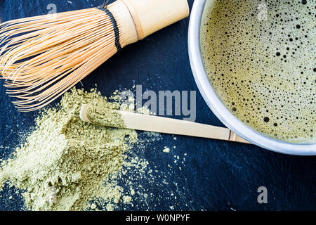 Eine Nahaufnahme von frisch zubereitete Matcha grüner Tee in einem Becher, Bambus Bambus whist, Löffel und grüner Tee Pulver Stockfoto