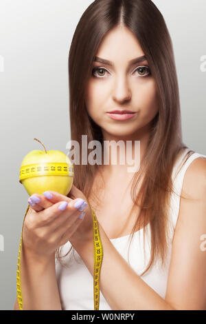 Diät. Fitness ein junges Mädchen hält sich an eine Diät und hält einen Apfel mit einem Maßband. Verlieren Sie Gewicht der Begriff der Schönheit und Gesundheit. Auf einem grauen Stockfoto