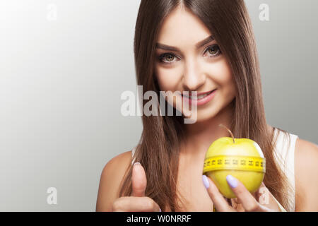 Diät. Fitness ein junges Mädchen hält sich an eine Diät und hält einen Apfel mit einem Maßband. Verlieren Sie Gewicht der Begriff der Schönheit und Gesundheit. Auf einem grauen Stockfoto