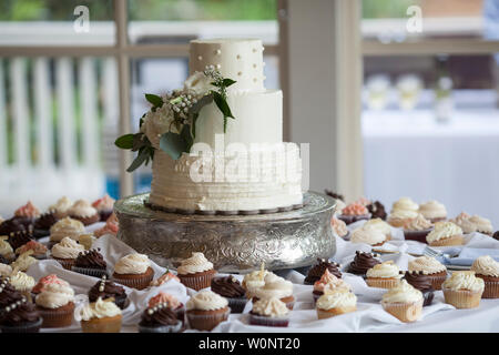 Schöne drei abgestufte Hochzeitstorte von Cupcakes auf Hochzeitsfeier umgeben. Stockfoto