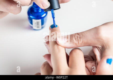 Eine Mutter malt die Hände ihre junge Mädchen mit blauen und rosa-Nagellack, gegen einen isolierten weißen Hintergrund gesehen
