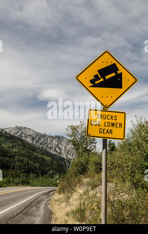 Schild, das die Lkw-Fahrer darauf hinweist, dass die Straße vor dem Fahrzeug steil und bergab sein wird. Berge und Wolken machen die Fahrt schön. Stockfoto